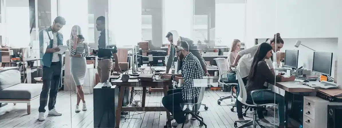 Diverse team collaborating in a modern office with natural light and a neutral color palette of white, gray, and beige. A tech-driven, creative environment representing innovation, inclusion, and social action ideal for showcasing teamwork, digital transformation, and corporate responsibility.