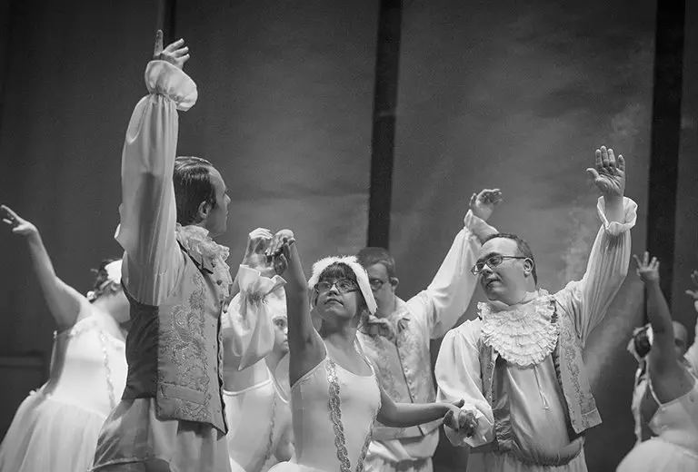 V15IONES de superación Personas con y sin discapacidad interpretan una coreografía clásica en blanco y negro, vistiendo trajes de época. La escena muestra una acción social que impulsa la inclusión a través del arte, destacando la diversidad y el talento en las artes escénicas.