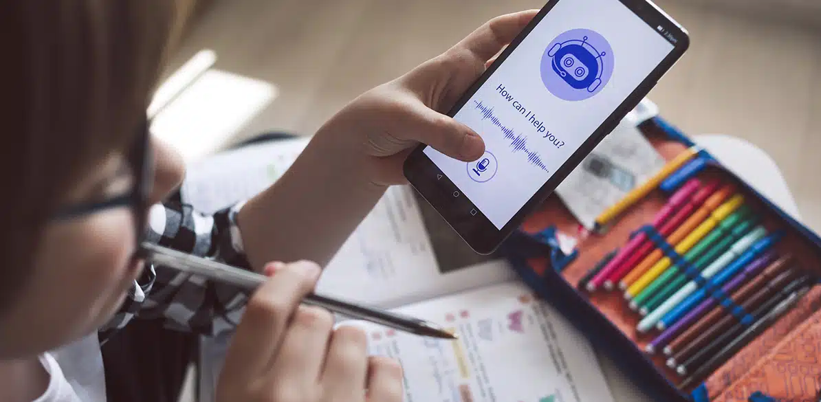 V Jornadas Salud Digital Niño usando un asistente de voz con inteligencia artificial en un smartphone mientras estudia, rodeado de material escolar.